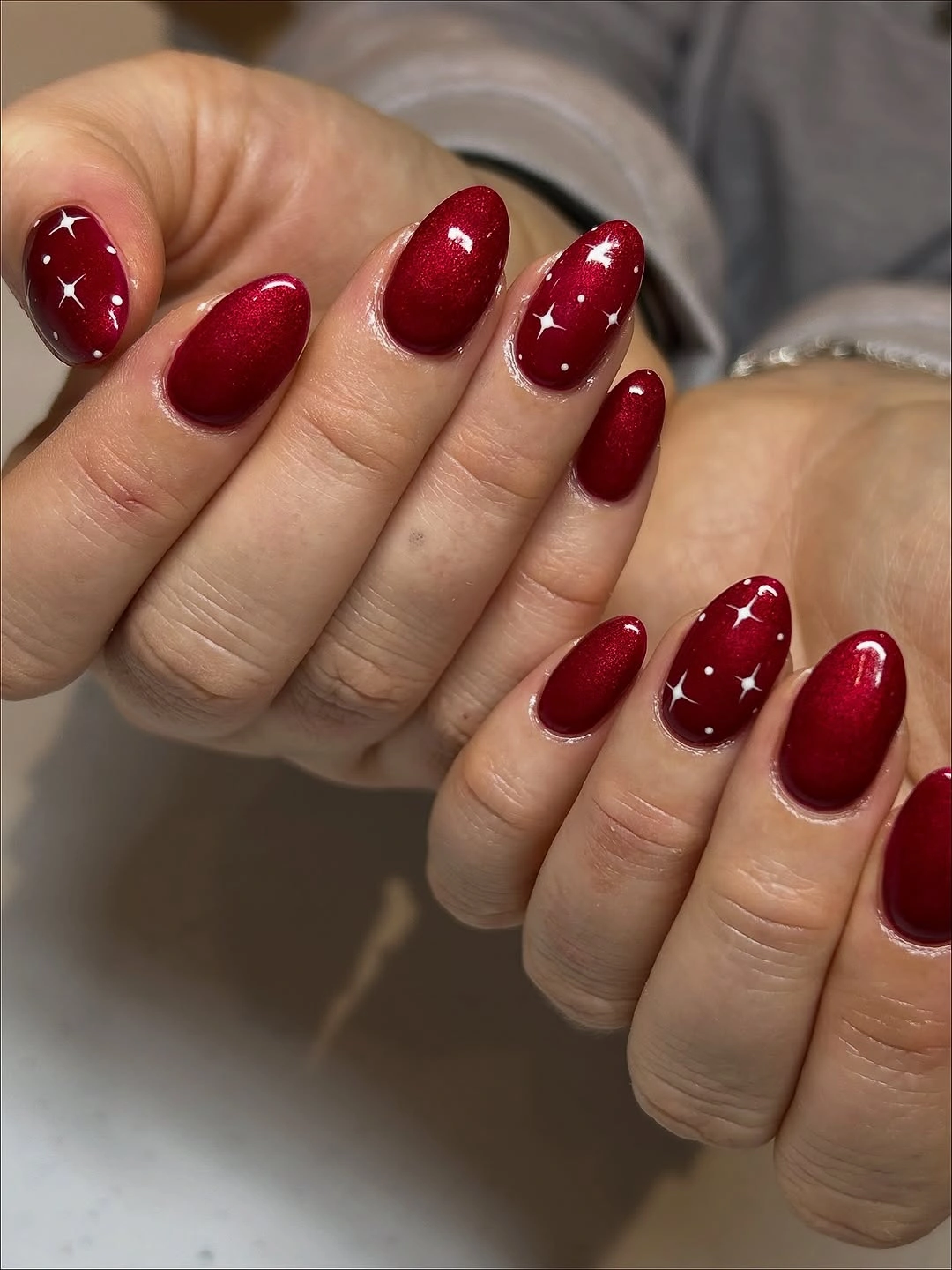 Rounded burgundy red shimmer nails with small white four-point stars