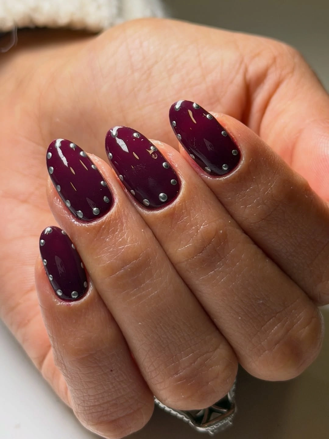 Short rounded plum-burgundy nails with silver-gray dots and fine diagonal marks