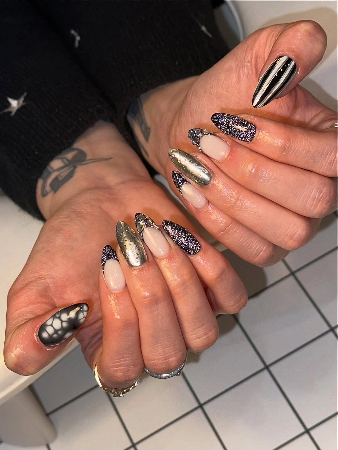 Long tapered nails with metallic-looking silver, dark glitter, and striped thumbs