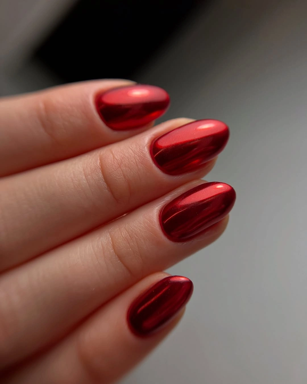 Medium almond nails with glossy metallic-looking cherry red and elongated reflections