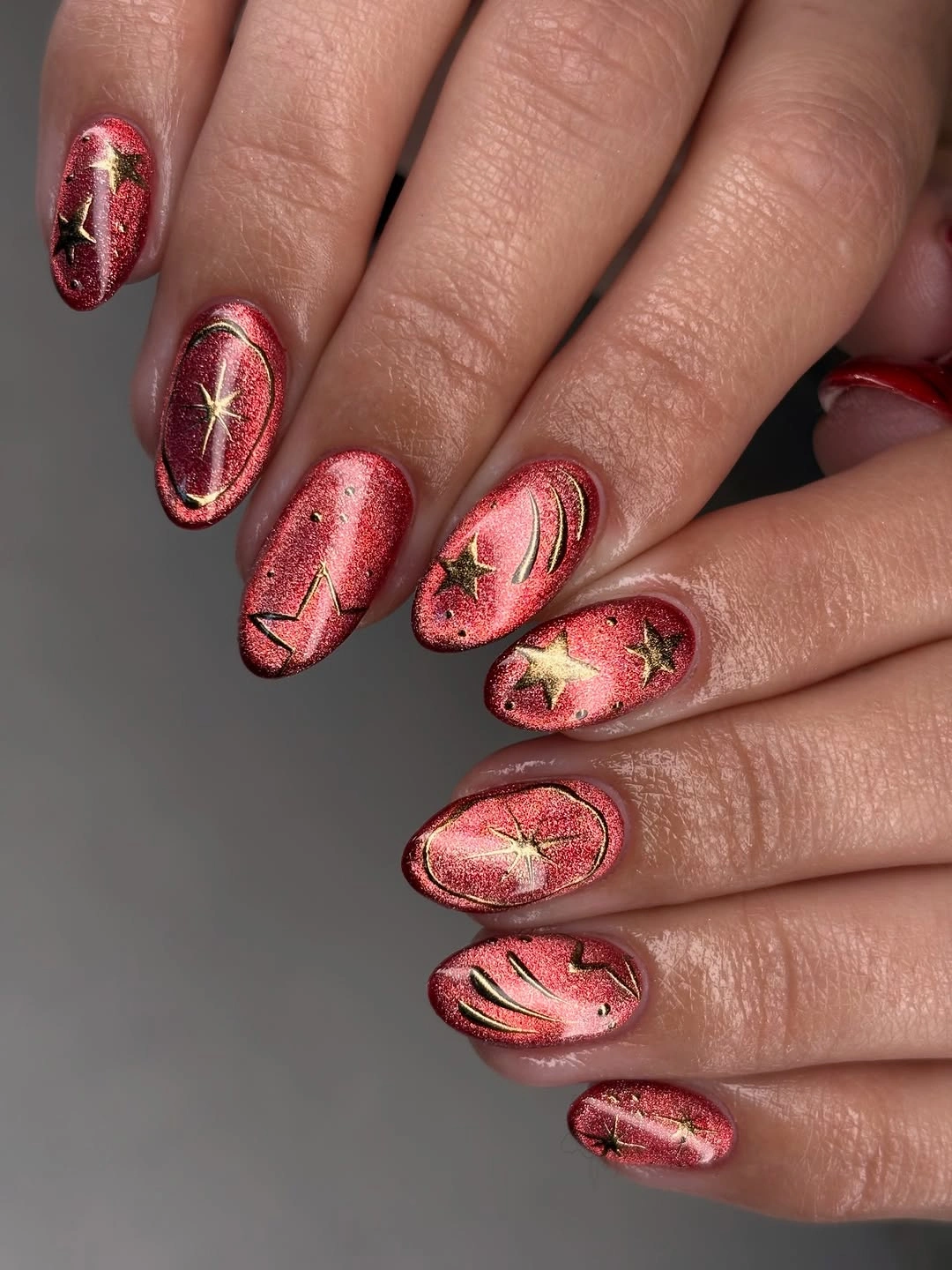 Almond nails with rosy red shimmer, gold-colored stars and curved lines