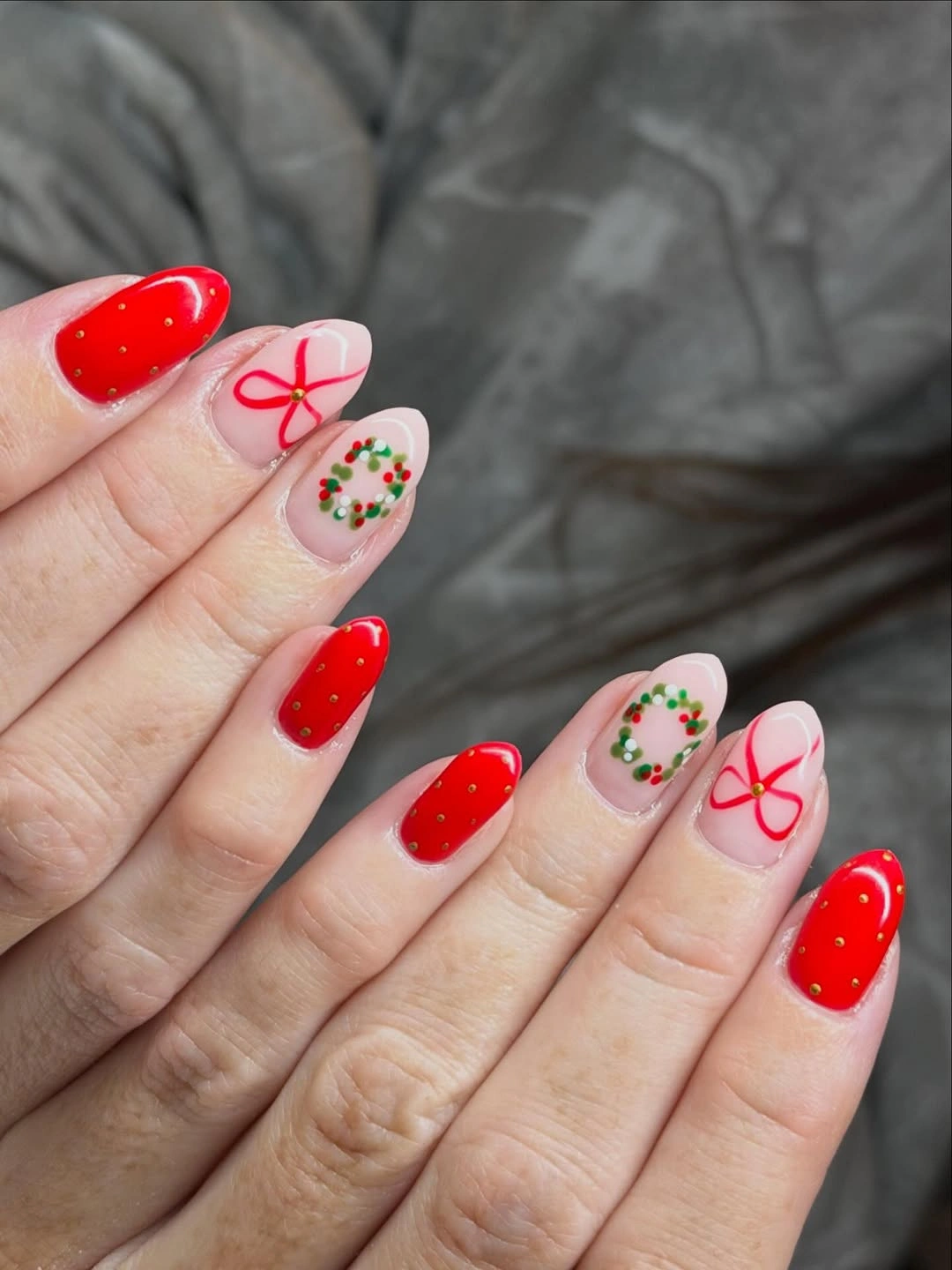 Glossy red almond nails with pink bow accents and dotted Christmas wreaths