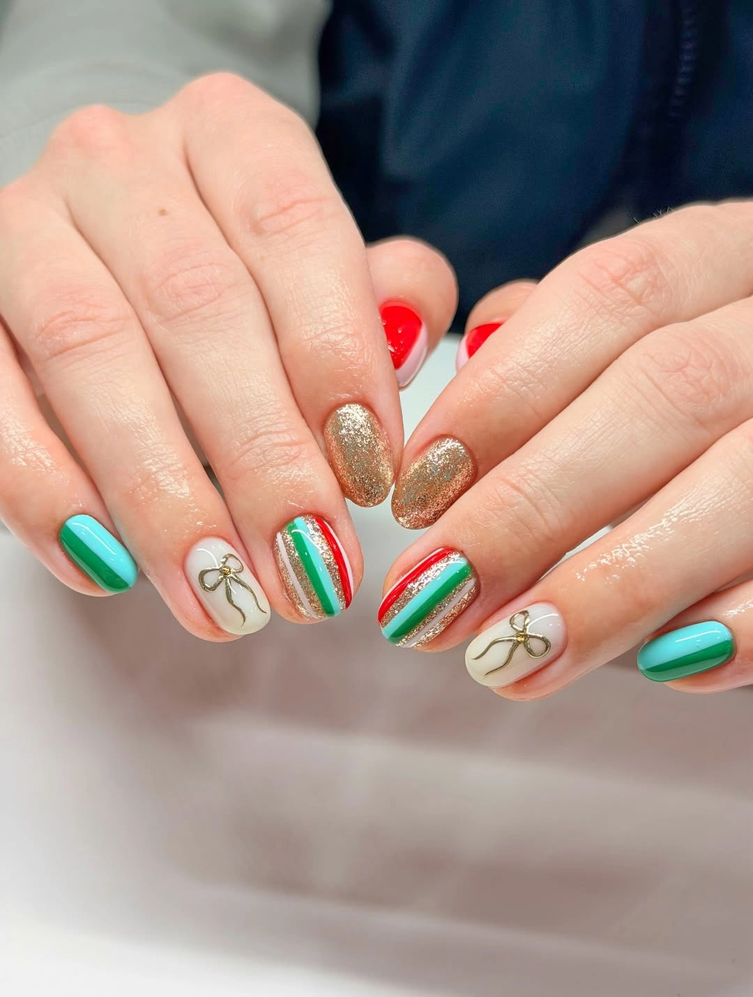 Short turquoise nails with gold glitter, striped accents and outlined bows