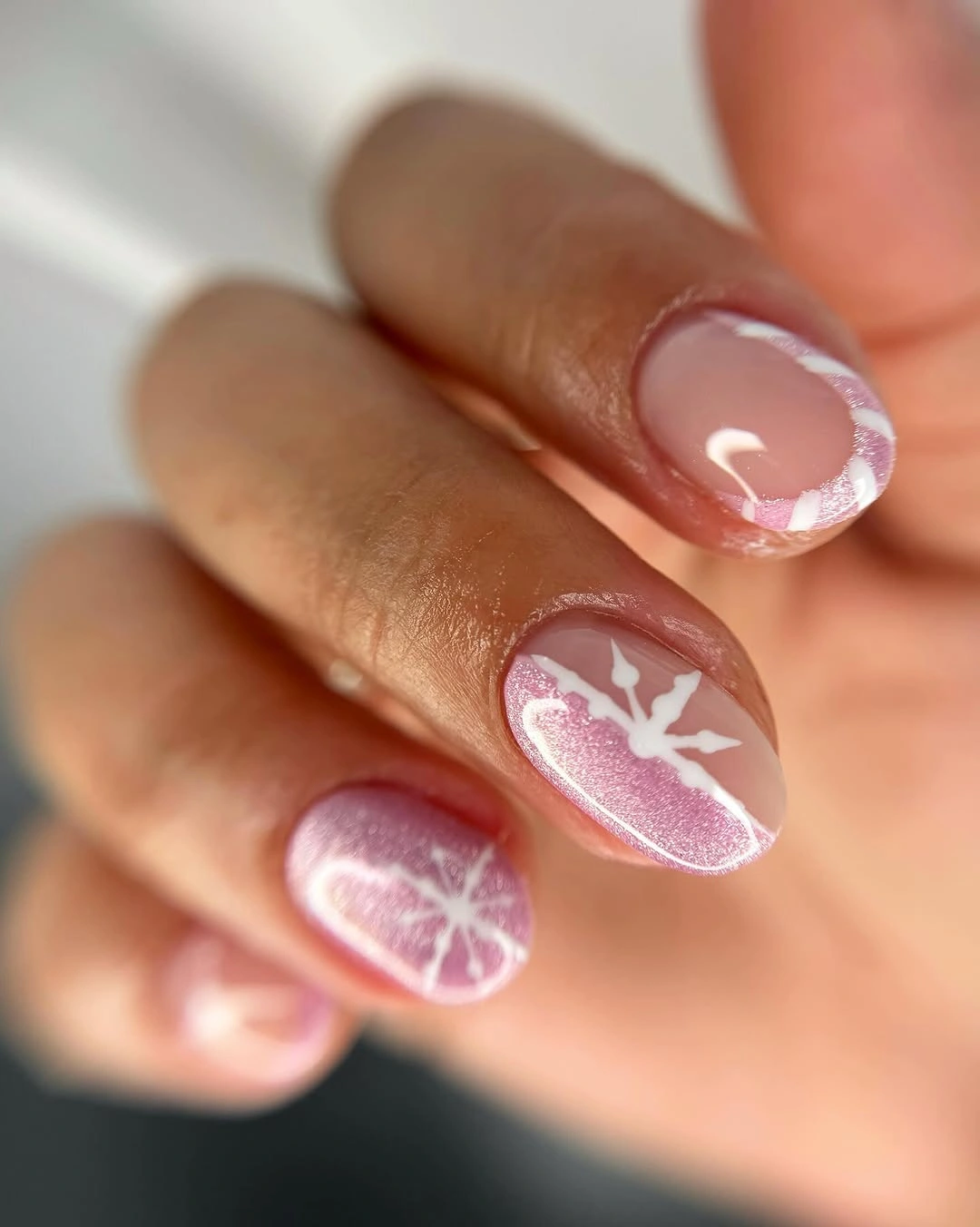 Short rounded pink nails with frosted shimmer and delicate white snowflake accents