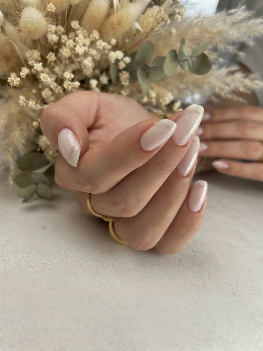 Milky-white almond nails with narrow white tips and fine gold curved accents