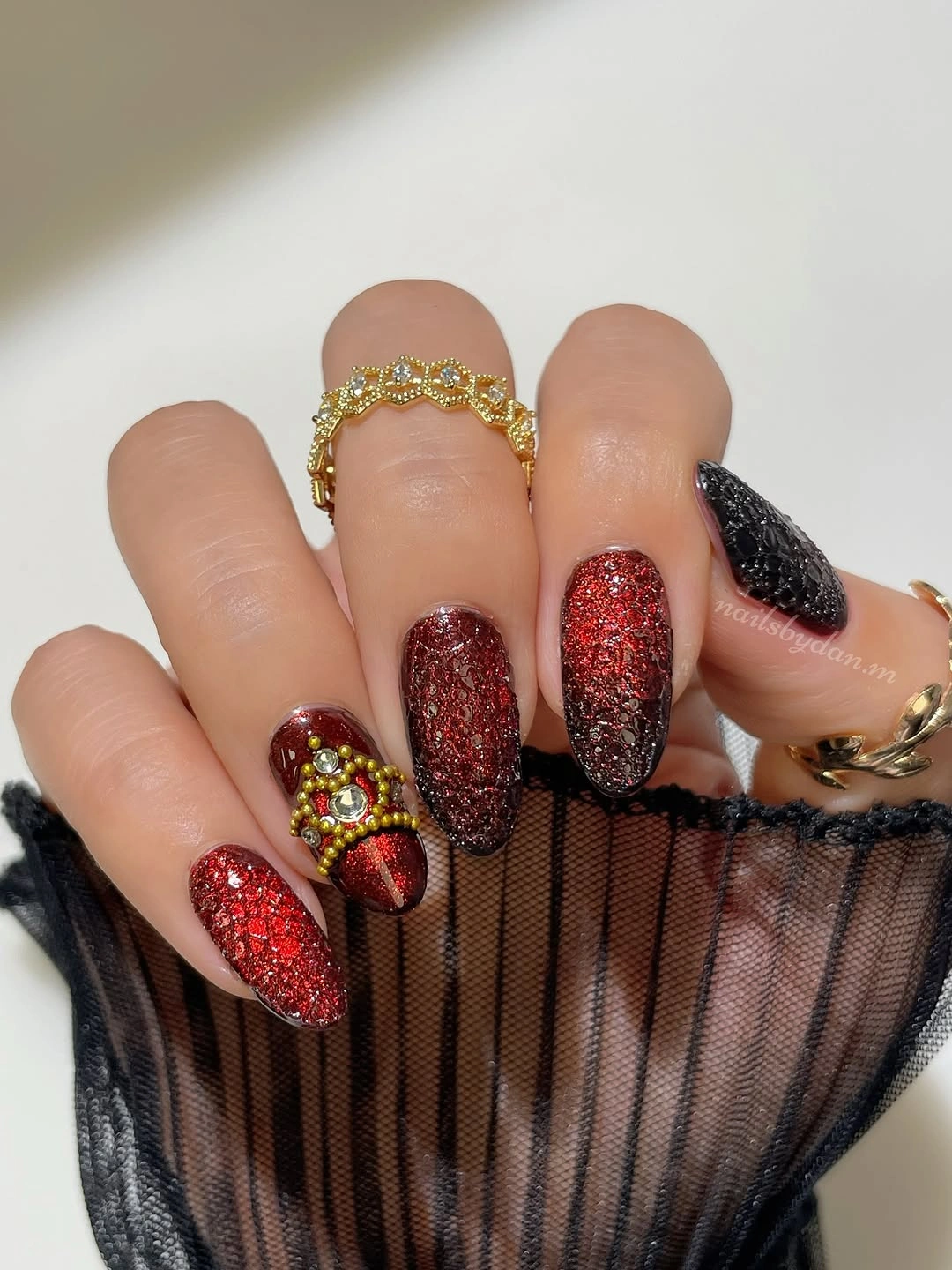 Long tapered nails with red glitter-looking coverage, black gradients, and gold-red embellishments