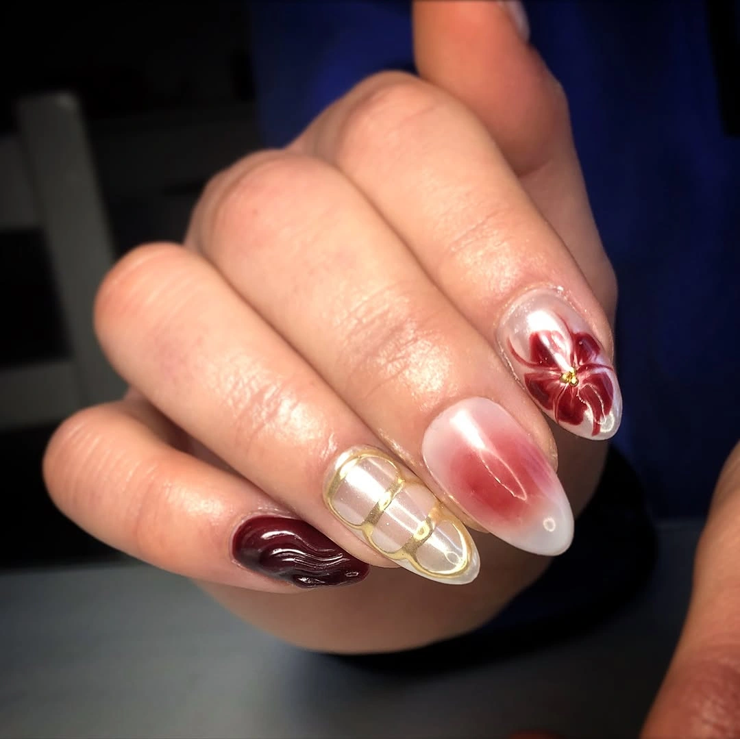 Almond nails with burgundy waves, gold grid lines, pink gradient, and painted flower