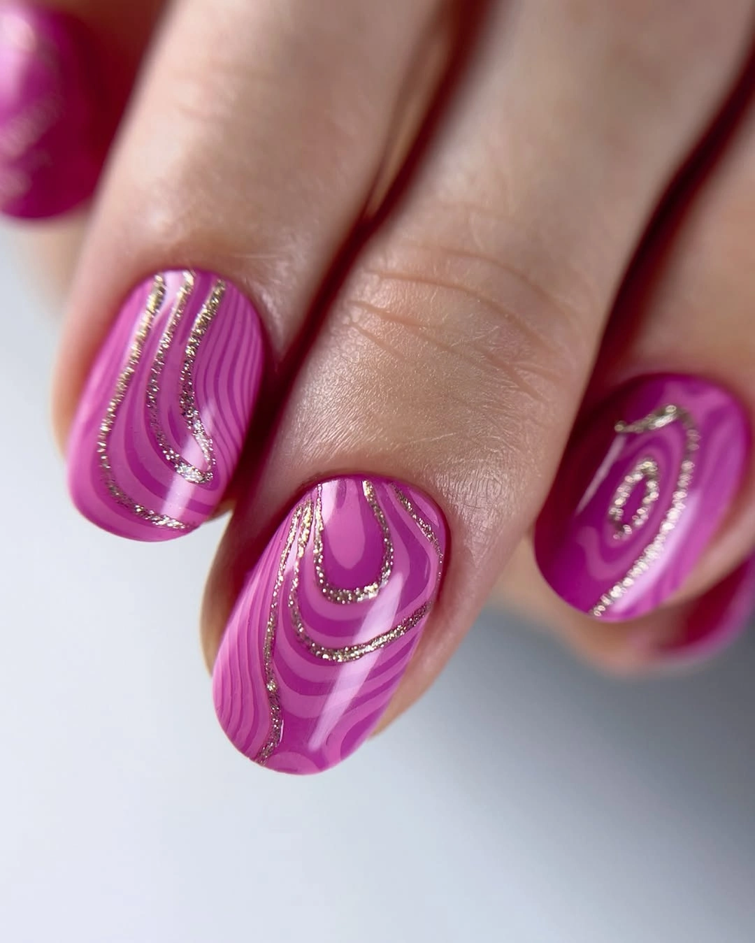 Long pink nails with purple swirls and thin gold-looking curved accents