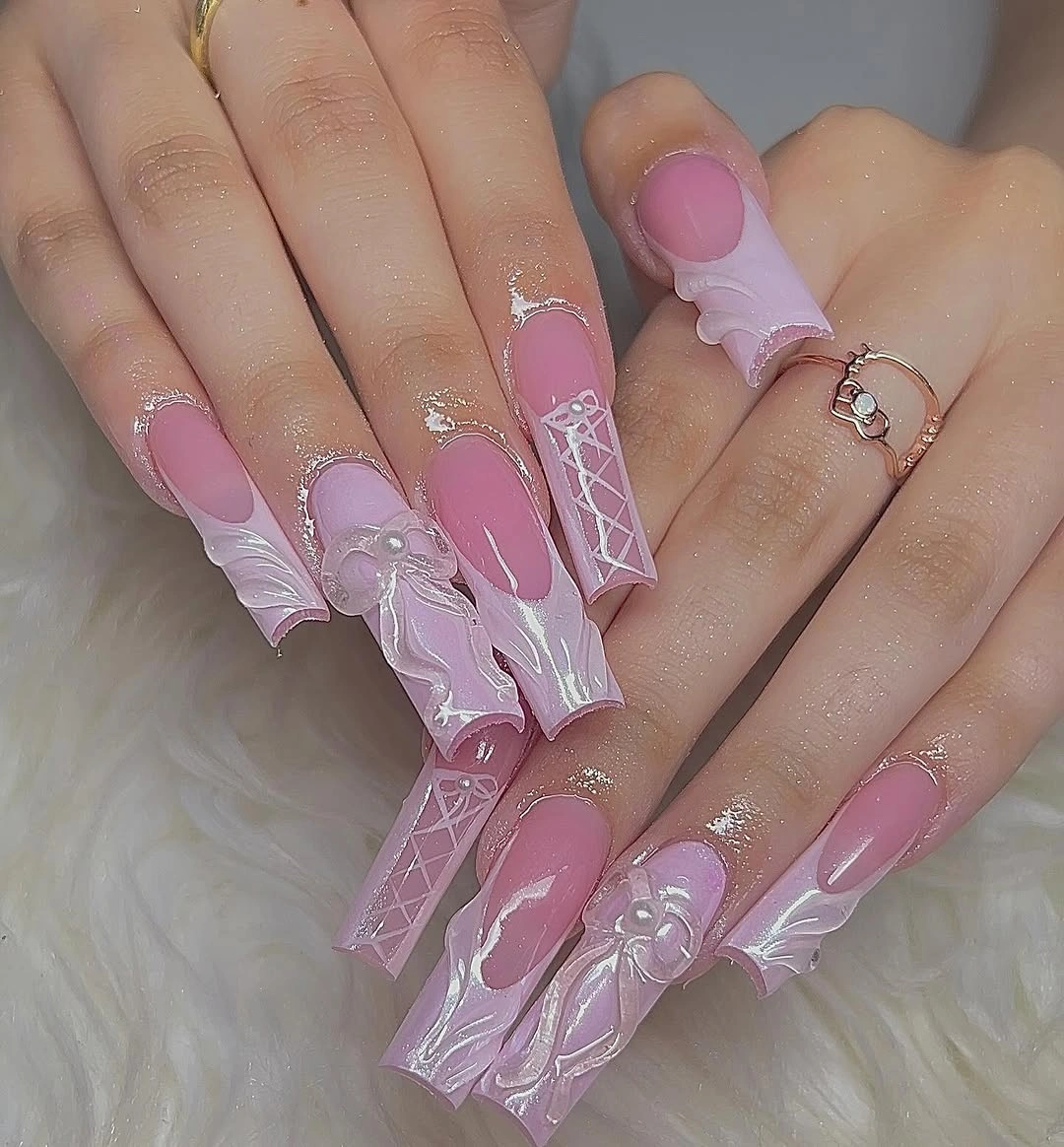 Extra-long pink nails with raised-looking bows, folded shapes, and crisscross lacing details