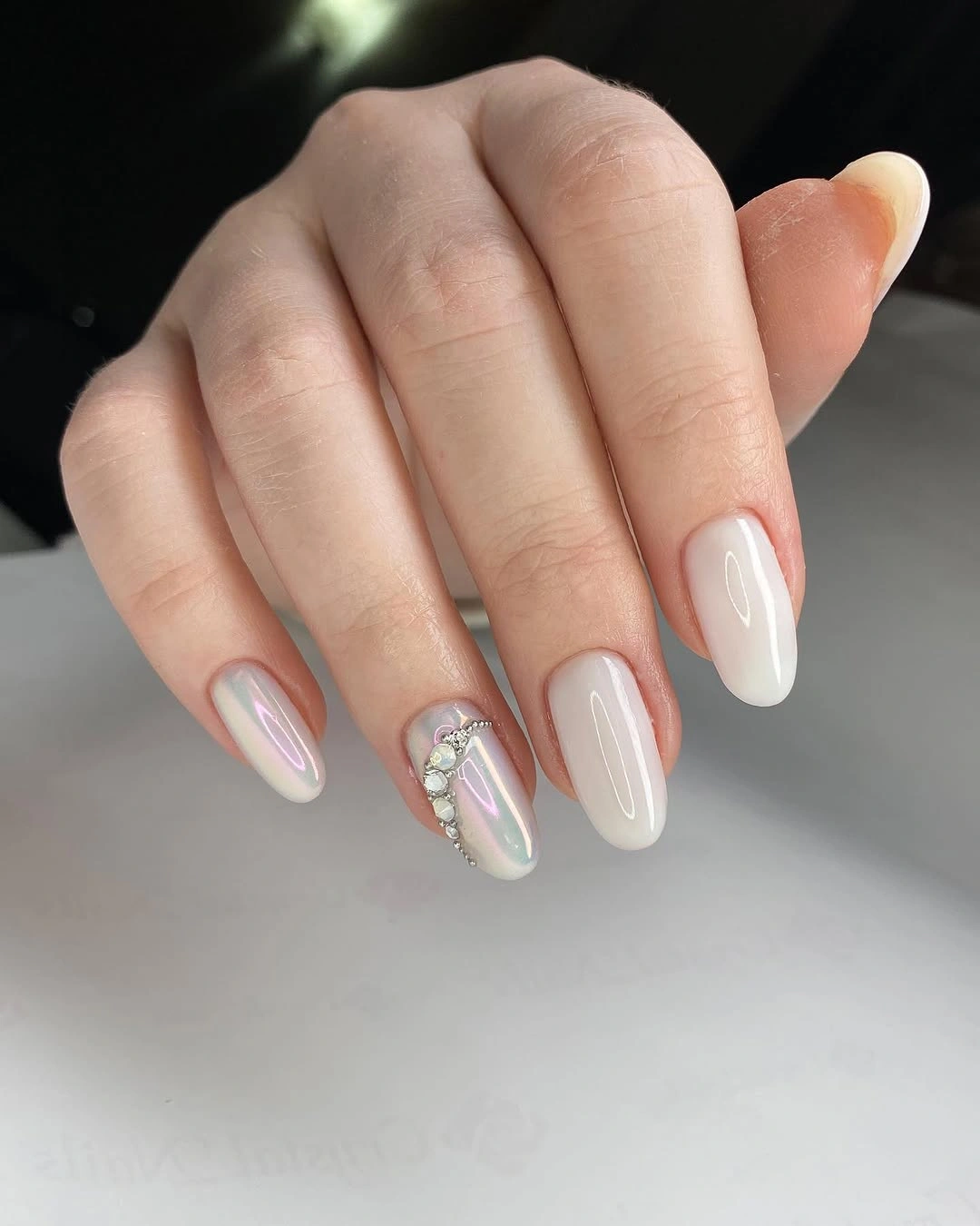 Milky white almond nails with subtle iridescence and curved gem-like accents