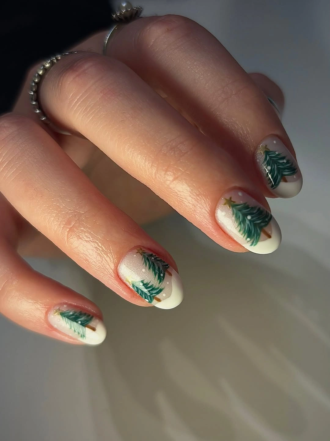 Creamy almond nails with painted green evergreen trees and white tips