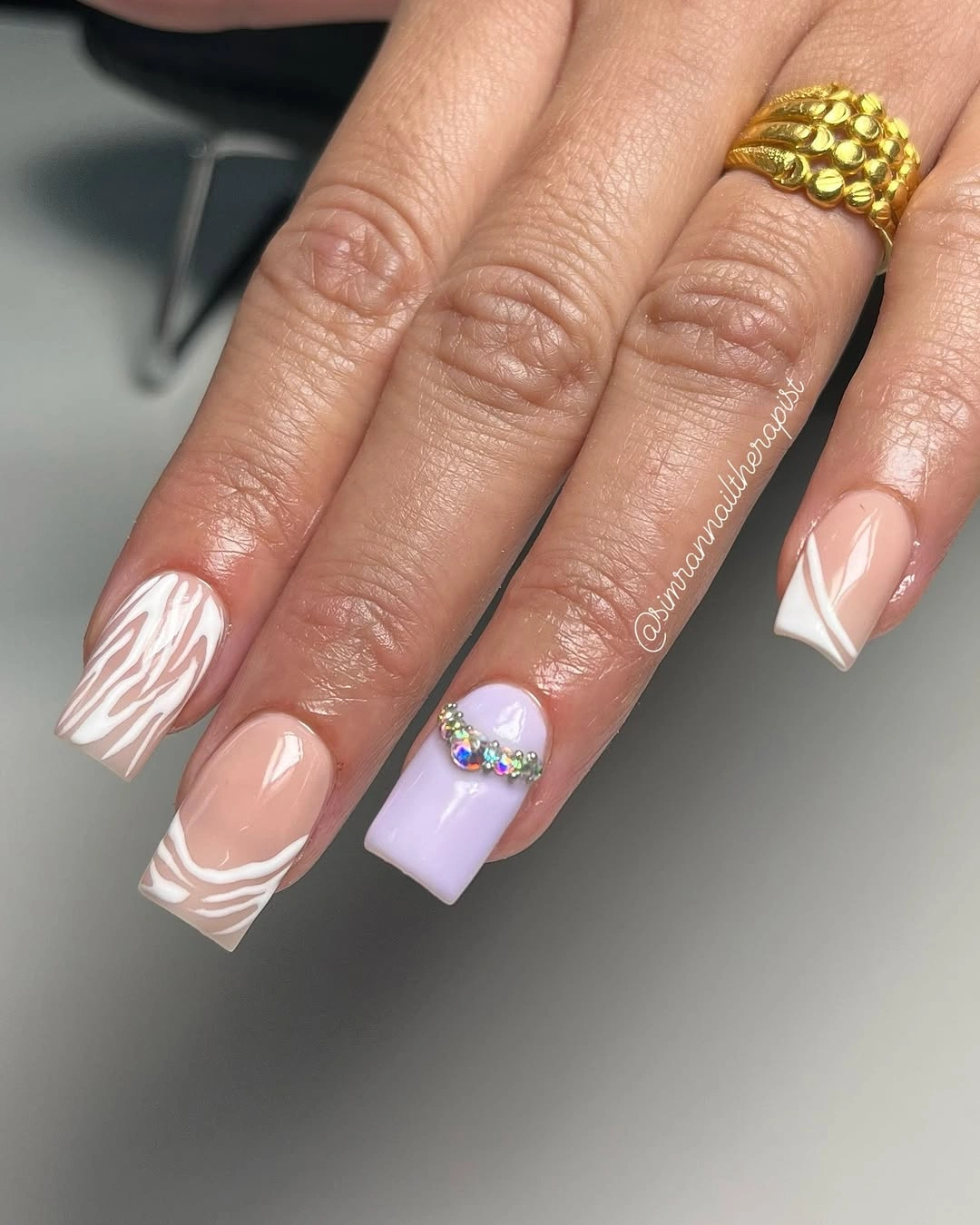 Long square nude-pink nails with white waves, lilac, and gem-like accents