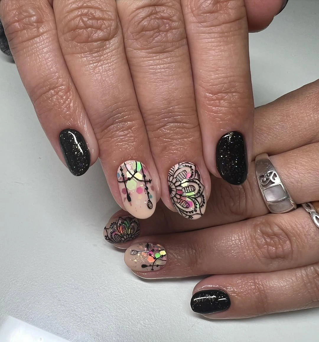 Short black glitter-looking nails with nude accents and colorful outlined motifs