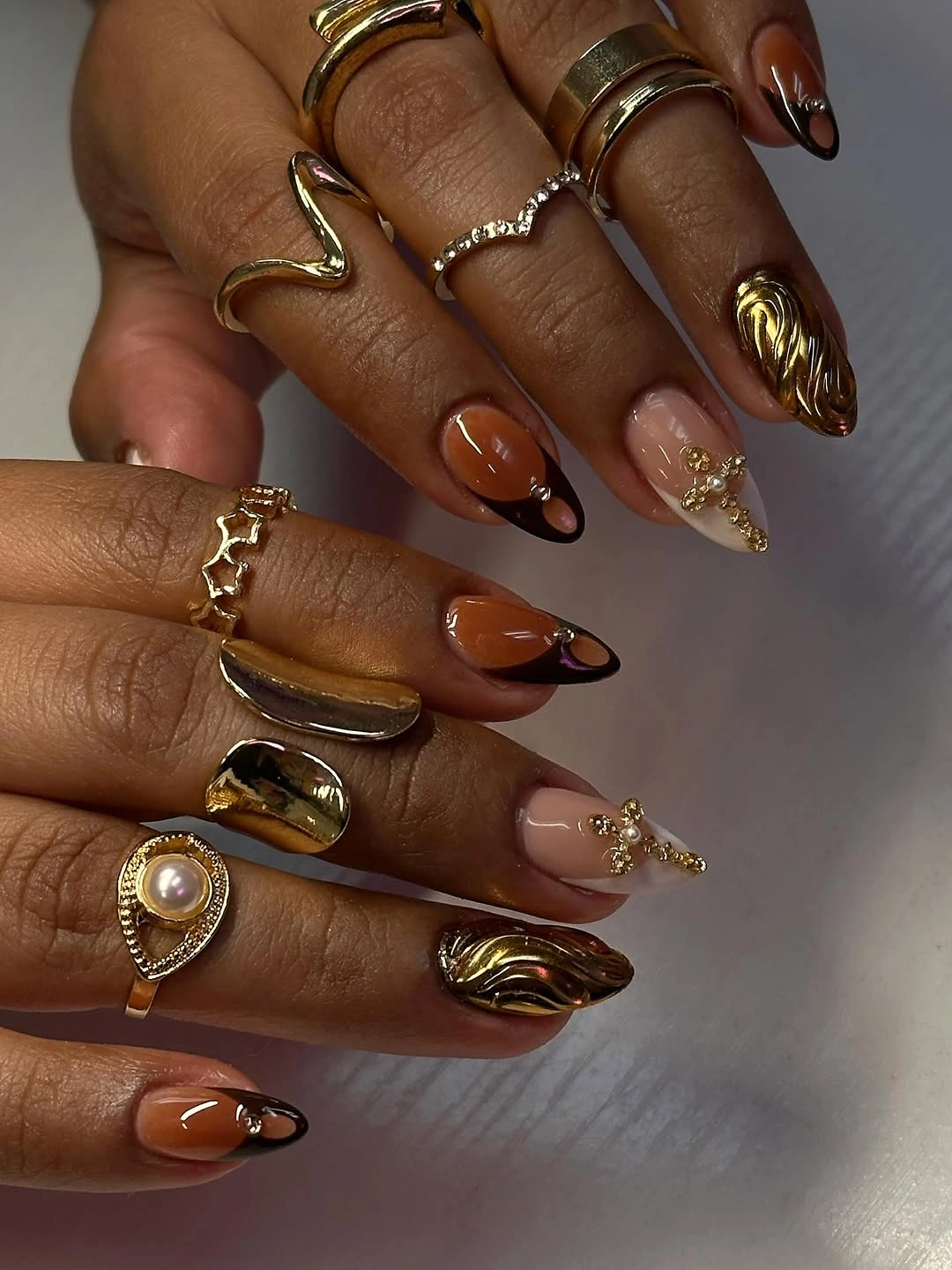 Long pointed nails with amber polish, black curves, and reflective gold waves