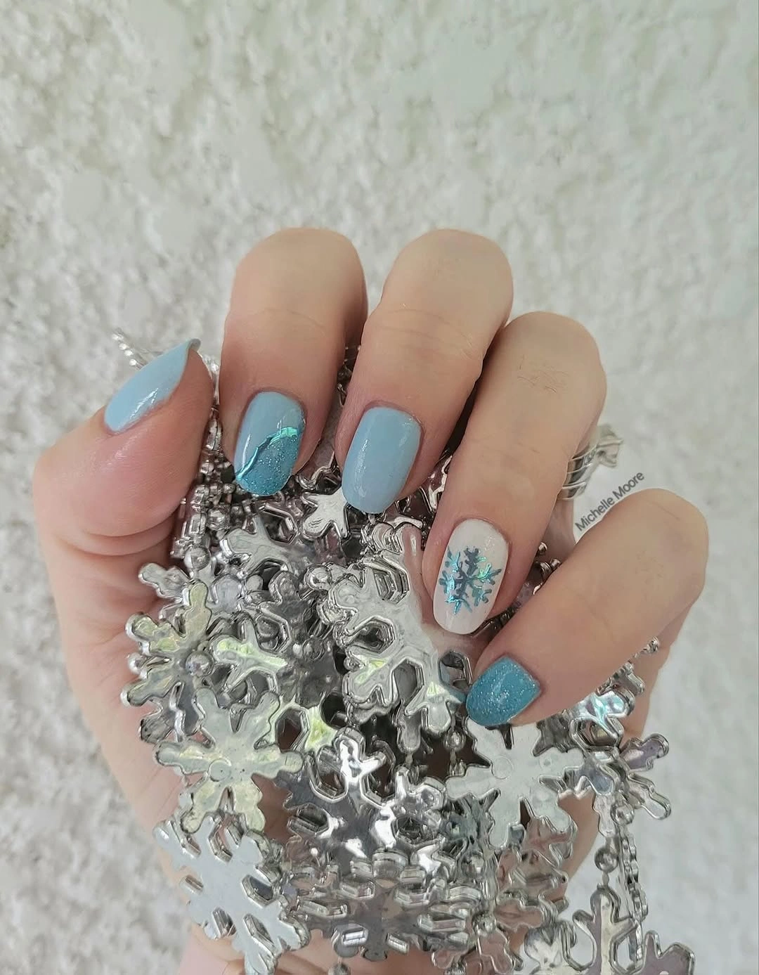 Pastel blue nails with turquoise glitter-looking accents and a blue snowflake
