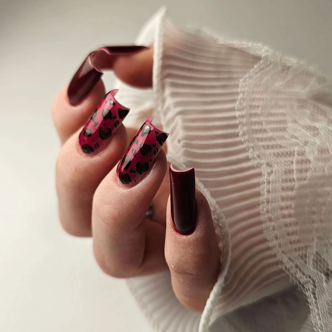 Long square nails combining glossy burgundy polish and pink accents with black spots