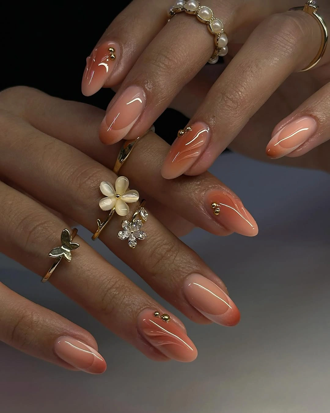 Warm peach almond nails with pale curved lines and gold bead-like accents