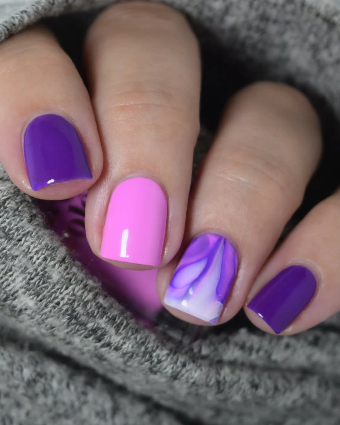 Short square-rounded nails in purple and pink with a wavy accent nail